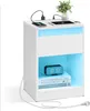 A white nightstand with integrated LED lighting, featuring a drawer, an open shelf, and a top surface with a smartphone and tablet charging. Produktbild-Vorschau