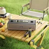A portable speaker and microphones are set up on a wooden table outdoors, with a camping chair and a kettle in the background. Podgląd zdjęcia produktu