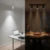 A split image showing a desk setup with a laptop on the left and a dining table with people on the right, both illuminated by spotlights. Produktbild-Vorschau