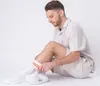A man is sitting on the floor and putting on a pair of white socks with orange stripes and a cocktail graphic. Produktbild-Vorschau