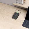 A smartphone with a power bank attached, placed on a wooden desk next to a keyboard and books on a shelf. Produktbild-Vorschau
