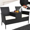 A black rattan garden bench with white cushions and a central table. The table has a glass of orange juice and fruit on it. An inset shows the storage compartment of the table open with books inside. Produktbild-Vorschau