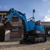 A blue mini excavator is parked on a gravel surface in front of a building under construction. Produktbild-Vorschau