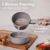 A hand is pouring liquid from a gray pot into a gray bowl, with ingredients like garlic and chili peppers in the background. Náhled obrázku produktu
