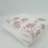 A folded white blanket with a pink rose pattern on a plain background. Produktbild-Vorschau