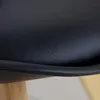 A close-up view of the edge of a black seat and a wooden leg of a chair. Produktbild-Vorschau