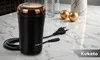 A black coffee grinder with a gold lid, placed on a marble surface with decorative gold spheres and vases. Podgląd zdjęcia produktu