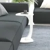 A white C-shaped side table with a cup and a phone on it, placed next to a dark gray sofa.