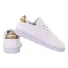 A pair of white Adidas Advantage women's sports shoes with gold accents. Podgląd zdjęcia produktu