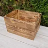 A wooden crate is placed on a light gray wooden surface with green foliage in the background. Produktbild-Vorschau