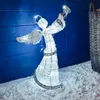 A lighted angel decoration sits in artificial snow in front of a blue wooden wall. Náhled obrázku produktu