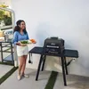 A woman is holding a tray of food next to a grill. Voir les images du produit