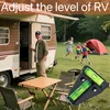 A family is enjoying a camping trip next to an RV. A table and chairs are set up, and a grill is visible. A level tool is in the foreground. Produktbild-Vorschau