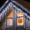 Icicle lights draped over the roofline of a wooden house with frosted windows. Anteprima dell’immagine prodotto