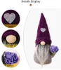 A decorative gnome with a purple hat and gray beard, holding a bouquet of purple flowers in a cone. Produktbild-Vorschau