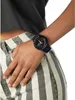 A person wearing a dark blue G-Shock watch on their wrist, with a close-up view of the watch and the person's striped pants. Voir les images du produit