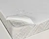 A close-up view of a white mattress protector with water droplets on it, partially lifted to show the mattress underneath. Produktbild-Vorschau