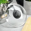 A glass pot lid with a black handle is placed on a countertop next to a stainless steel pot. Podgląd zdjęcia produktu