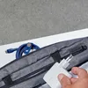 A hand holding a white Belkin charger near a gray bag with a blue cable inside. Produktbild-Vorschau