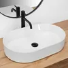 A white oval countertop sink with a black faucet and drain is placed on a wooden surface, with a circular mirror reflecting the faucet in the background. Náhľad obrázku produktu