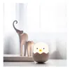 A small, egg-shaped chick lamp sits on a surface in front of two elephant figurines. Produktbild-Vorschau