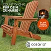 A wooden Adirondack chair is shown outdoors with lush green foliage in the background. A circular inset shows a person reading by a fireplace. Produktbild-Vorschau