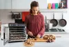 A woman is preparing mushrooms in a kitchen next to a food dehydrator. Podgląd zdjęcia produktu