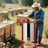 A beekeeper in a protective suit is using a honey extractor in a field with beehives. Produktbild-Vorschau