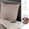 A close-up of a beige pillow and bedding, with informational icons and text on the right side. Produktbild-Vorschau