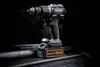 A Dewalt cordless drill with a battery pack attached, resting on a dark, textured surface with metal rods in the foreground and background. Voir les images du produit