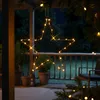 A star-shaped LED light decoration hangs from a tree branch on a porch at night. Produktbild-Vorschau