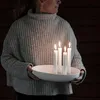 A person holding a white ceramic candle holder with four lit white candles. Produktbild-Vorschau