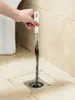 A hand is using a drain cleaning brush to remove hair from a floor drain. Produktbild-Vorschau