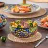 A table setting with a colorful ceramic bowl filled with pasta and meat, a plate with food in the background, and a lime on a jute placemat. Produktbild-Vorschau
