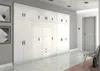 A long, white wardrobe with multiple doors and drawers is shown in a hallway with a door and a chair in the background. Produktbild-Vorschau