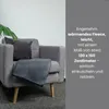 A dark gray fleece blanket is draped over a gray armchair, with a dark gray cushion and a green plant leaf visible. Produktbild-Vorschau