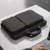 A black laptop bag with two compartments is placed on a white surface next to a laptop. A person's hand is visible typing on the laptop. Produktbild-Vorschau