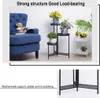 A blue armchair and a black metal plant stand with potted plants are shown in a room setting. Another white plant stand with plants is in the background. Náhľad obrázku produktu