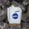 A white BigBag filled with stones, placed on a wooden pallet, with a background of large stones. Produktbild-Vorschau