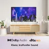 A television set is displayed on a wooden cabinet, with sound wave graphics overlayed on the screen and in front of the television. The bottom of the image shows logos for Dolby Audio and DTS HD, along with text. Produktbild-Vorschau