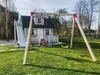 A backyard scene with a children's playhouse, slide, and swing set. Anteprima dell’immagine prodotto