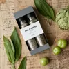 A gift box of salt and pepper spices is arranged on a wooden surface with fresh greens and an artichoke. Produktbild-Vorschau