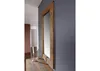 A mirror with a wooden frame is leaning against a gray wall, with a wooden table and two candlesticks in the foreground. Anteprima dell’immagine prodotto