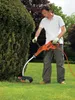 A man is using an electric trimmer to trim a large bush in a garden. Náhľad obrázku produktu