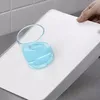 A hand is holding a white cutting board with a glass of blue liquid on it. Voir les images du produit