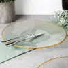 A glass charger plate with a gold rim, set on a table with cutlery and a napkin. Podgląd zdjęcia produktu