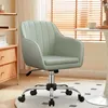 A light green office chair with a chrome base and wheels is shown in a room with wooden blinds and a shelf in the background. Produktbild-Vorschau