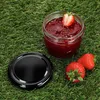 A jar of strawberry jam with a lid and strawberries on grass. Podgląd zdjęcia produktu