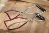 A pair of jar lifting tongs with red coated arms and black handles, resting on a wooden surface. Produktbild-Vorschau