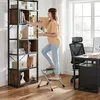 A woman is using a step stool to reach items on a bookshelf in an office setting. Produktbild-Vorschau